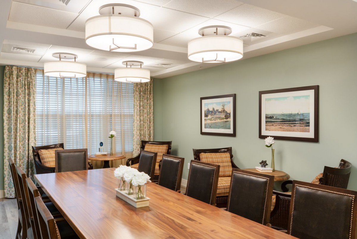 A well-lit conference room with a large wooden table and several chairs, decorated with framed art on the walls.