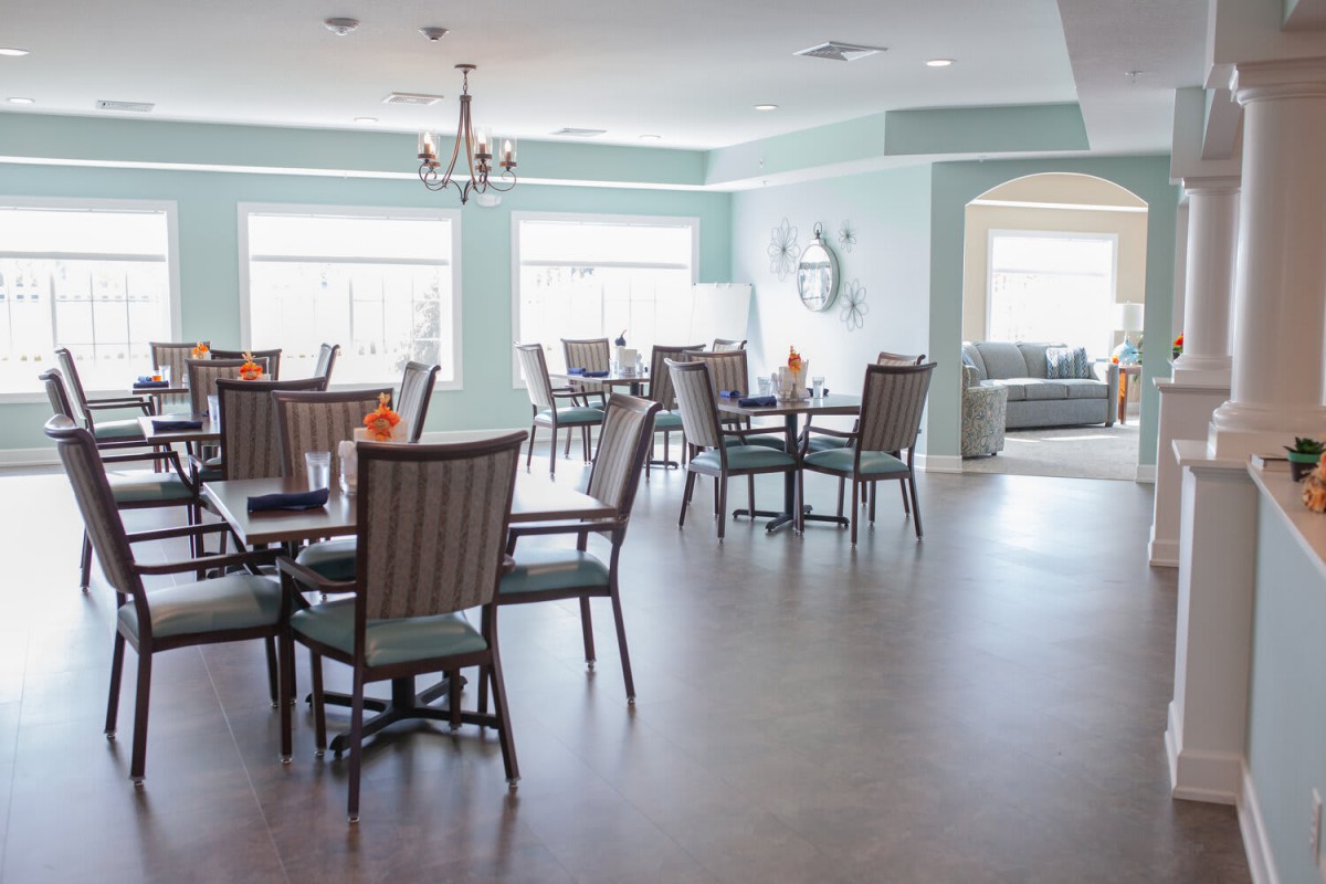 A modern and spacious dining room with multiple tables and chairs, well-lit by large windows.