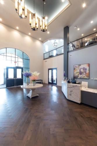 A spacious and modern lobby with a high ceiling, featuring a reception desk, decorative flowers, and a chandelier.