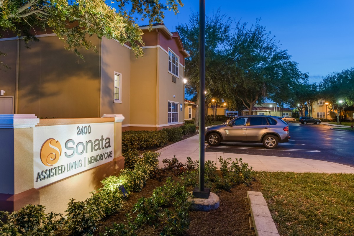 An evening view of an apartment complex with a well-lit entrance and parking area.