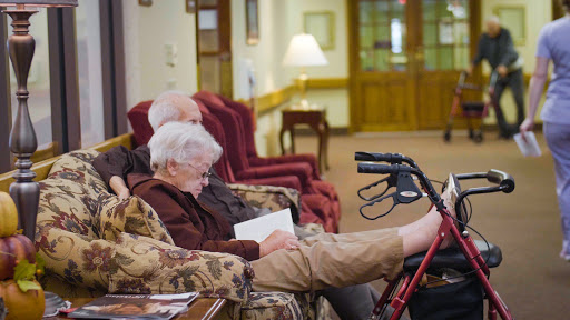 Two seniors relaxing in a cozy common area, one enjoying a book.