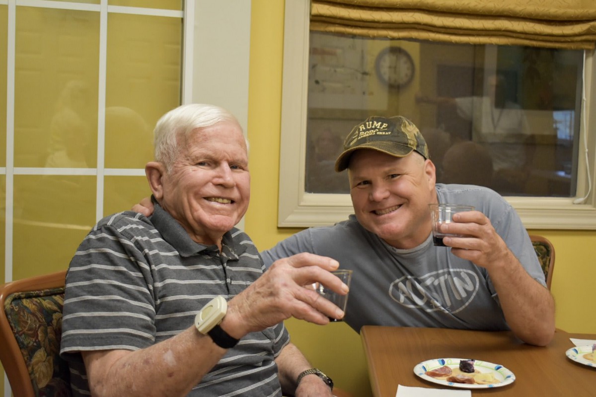 Two friends enjoying a drink together while smiling indoors.