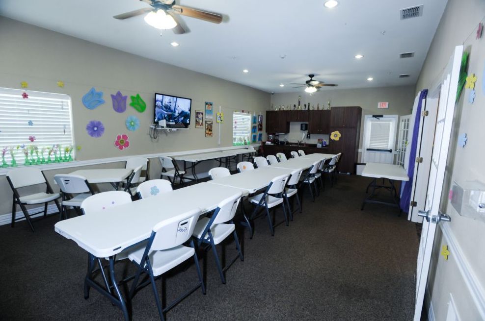 A spacious conference room with long tables and chairs, ideal for meetings and presentations, featuring ceiling fans and colorful wall decorations.