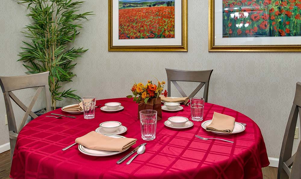 A dining table is elegantly set with a red tablecloth, complete with plates, glasses, napkins, and a central floral arrangement.