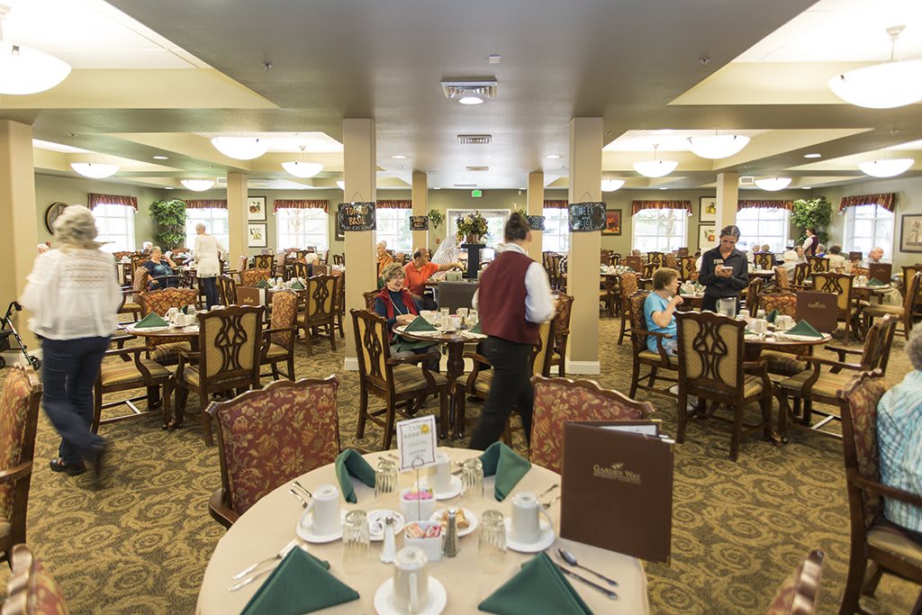 A bustling restaurant dining room with neatly set tables and waitstaff attending to guests.