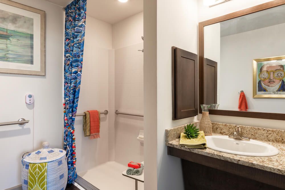 A modern bathroom with a shower, sink, and mirror, featuring colorful decor.