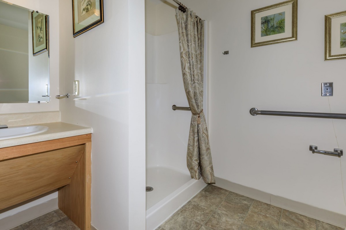 A bathroom with a shower area, curtain, and safety grab bars.
