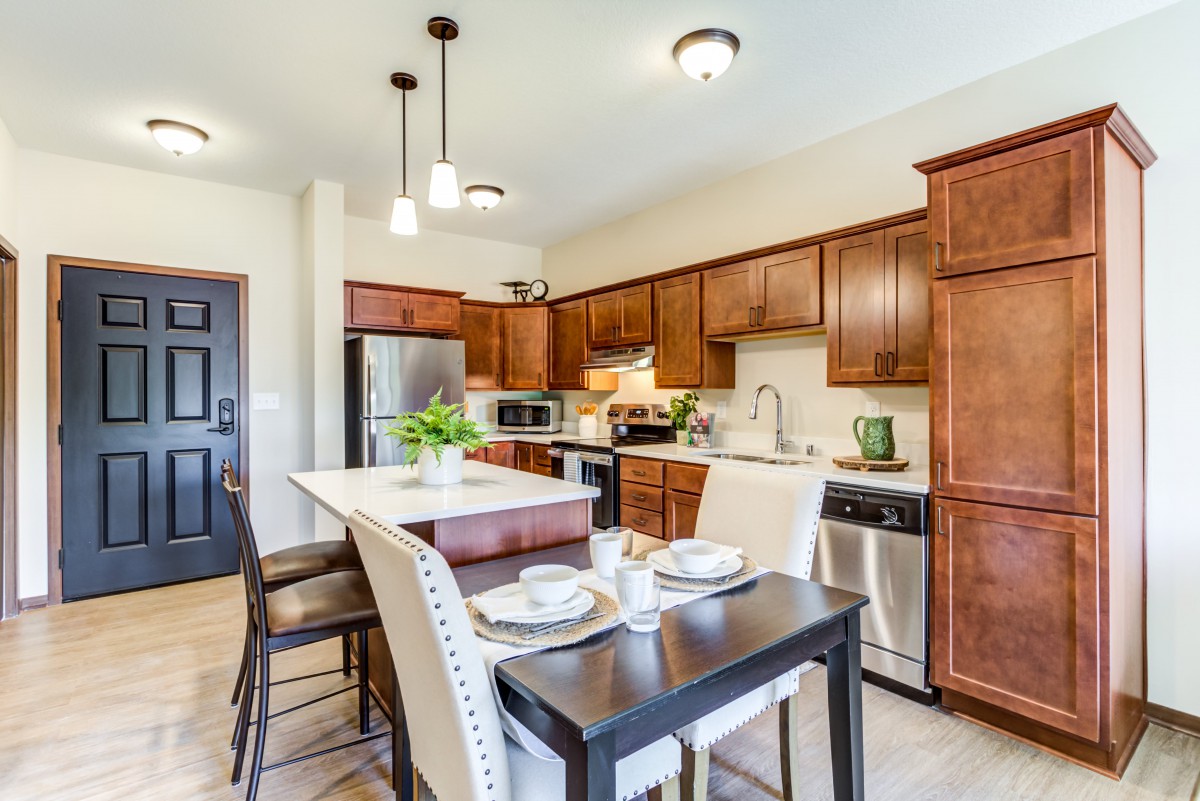A modern kitchen with wooden cabinets, a central island, and stainless steel appliances, featuring a cozy dining area.