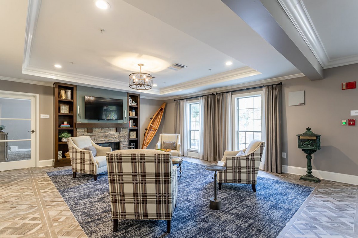 A cozy living room with plaid armchairs arranged around a coffee table, featuring a fireplace and built-in bookshelves.