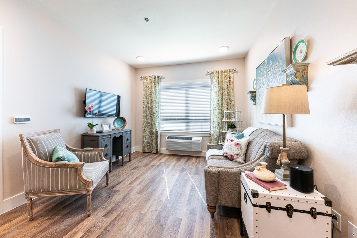 A cozy living room with modern decor, featuring comfortable seating, a television, and a large window with curtains.