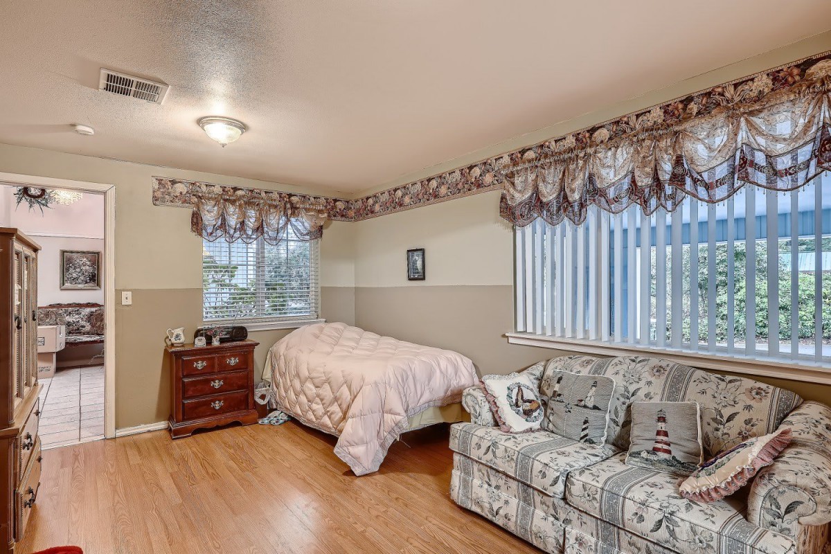 A cozy bedroom with a single bed, sofa, and wooden flooring, featuring two windows with decorative drapes.