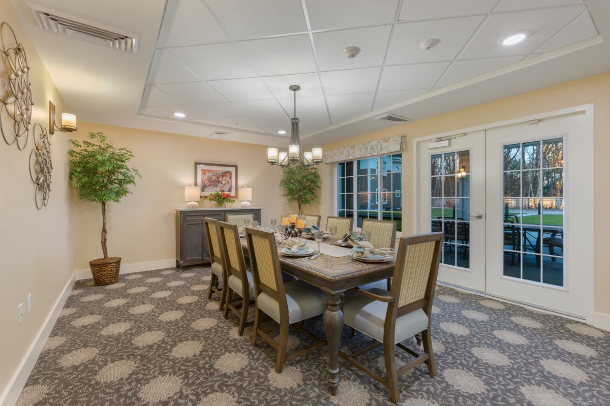 A well-decorated dining room featuring an elegant table setting with a chandelier, surrounded by comfortable chairs and lush greenery.