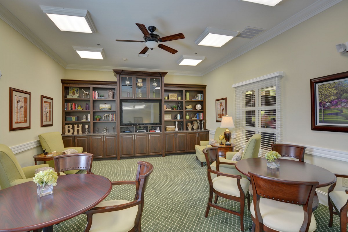 A cozy library room featuring bookshelves, tables, chairs, and warm lighting.