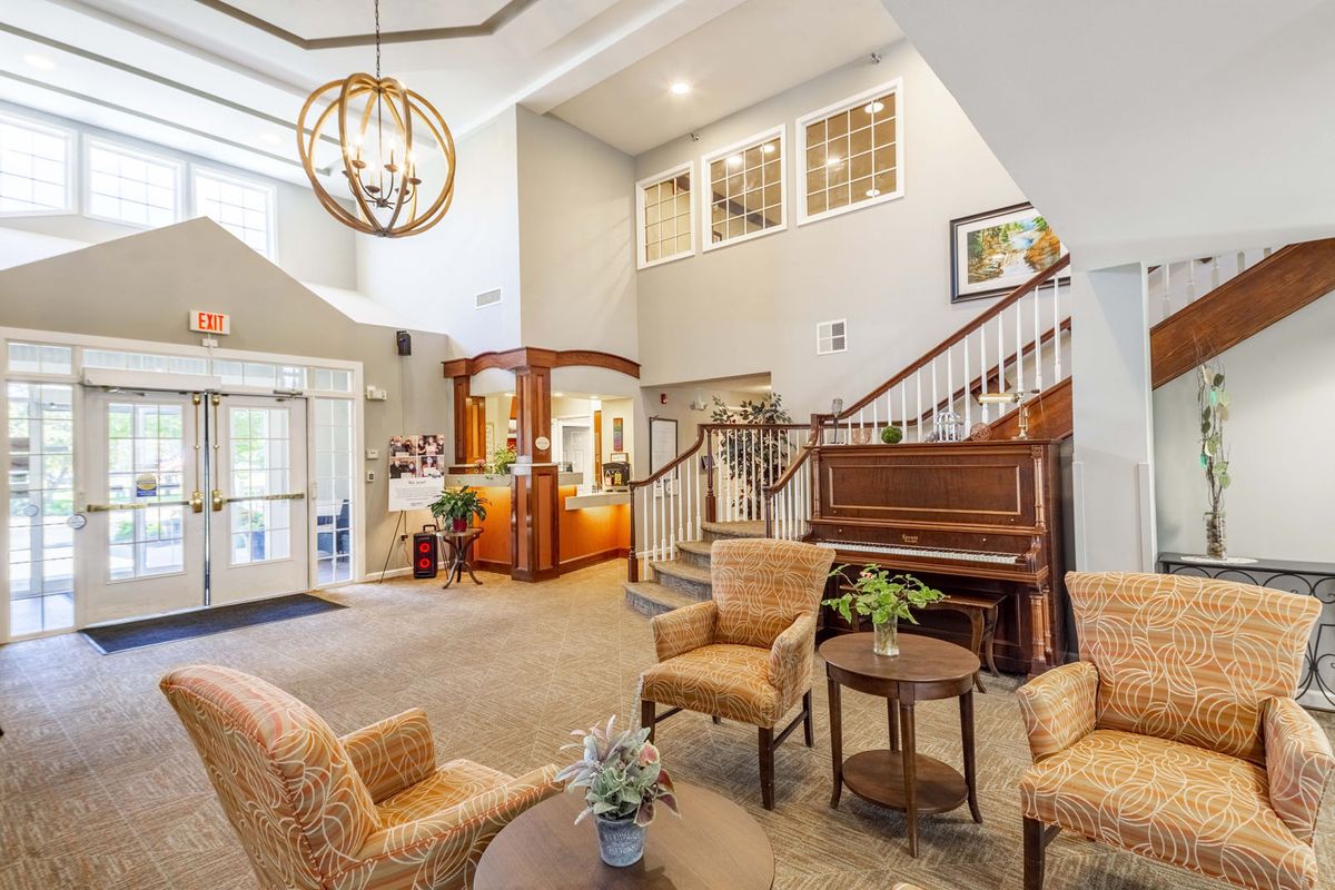A cozy living area with comfortable seating, a piano, and a staircase under a chandelier.