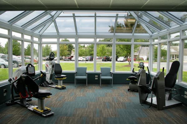 A well-lit gym with cardio machines and large windows providing a view of the outside.