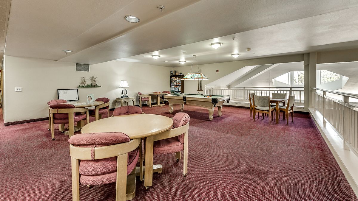A spacious lounge area with tables and chairs, featuring a carpeted floor and bright lighting.