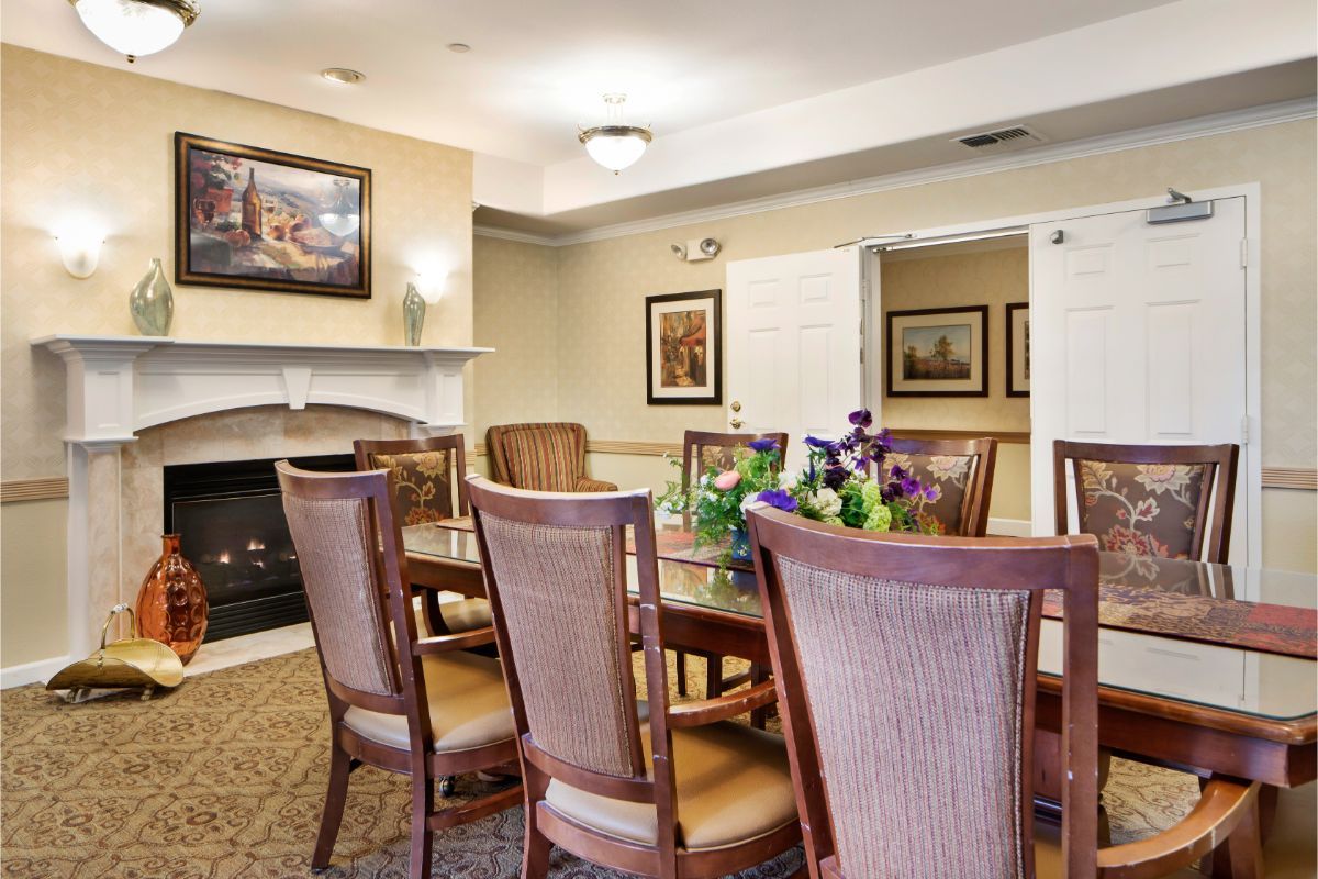 A cozy dining room with a table surrounded by chairs, adorned with flowers and decorative paintings on the walls.