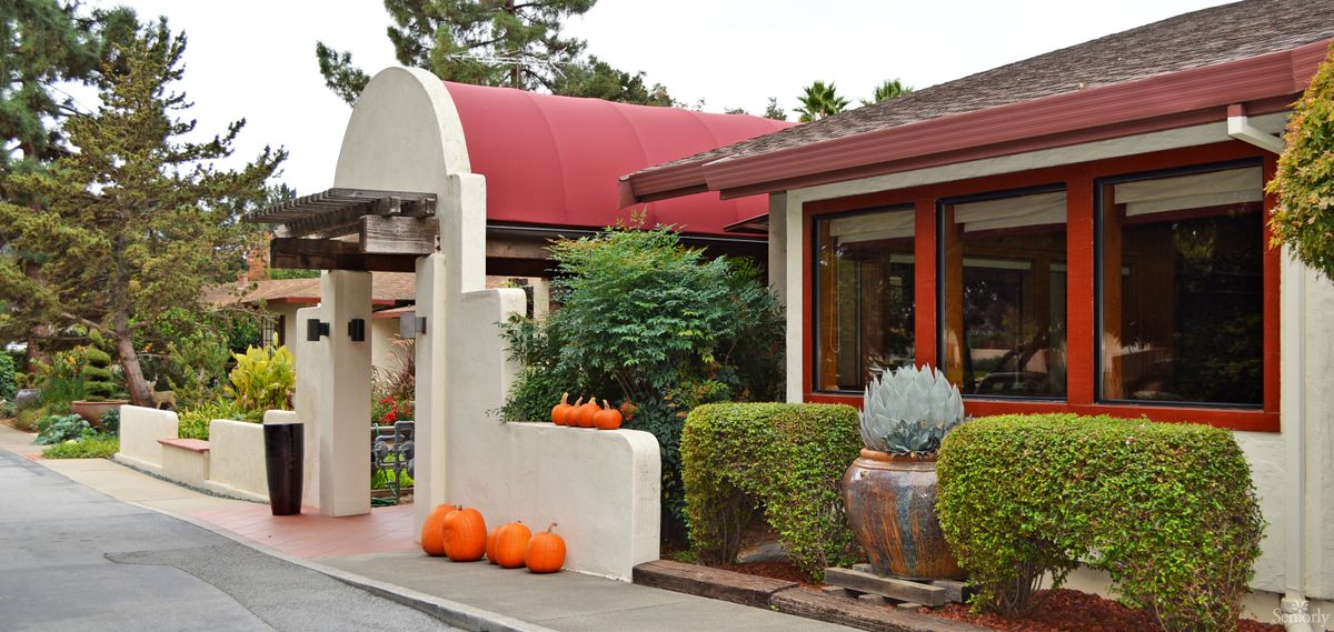 An inviting restaurant entrance decorated with pumpkins and greenery, showcasing a cozy autumn ambiance.