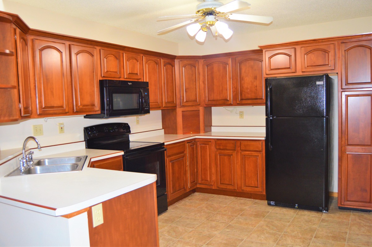 A spacious kitchen with wooden cabinets, modern appliances, and a ceiling fan.