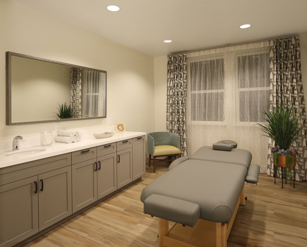 A serene massage room featuring a comfortable massage bed, modern cabinetry, and soft lighting.