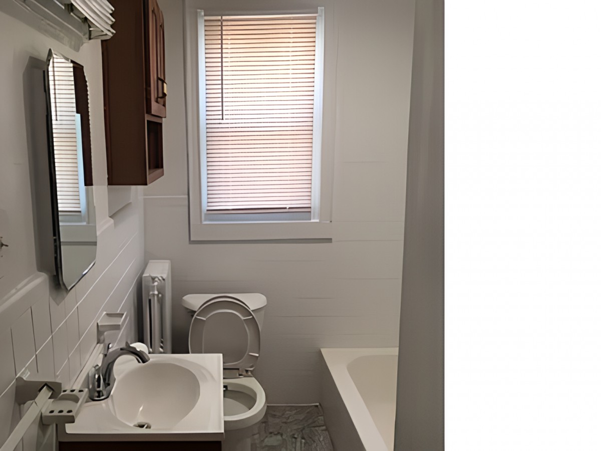 A small bathroom featuring a sink, toilet, and bathtub with a window covered by blinds.