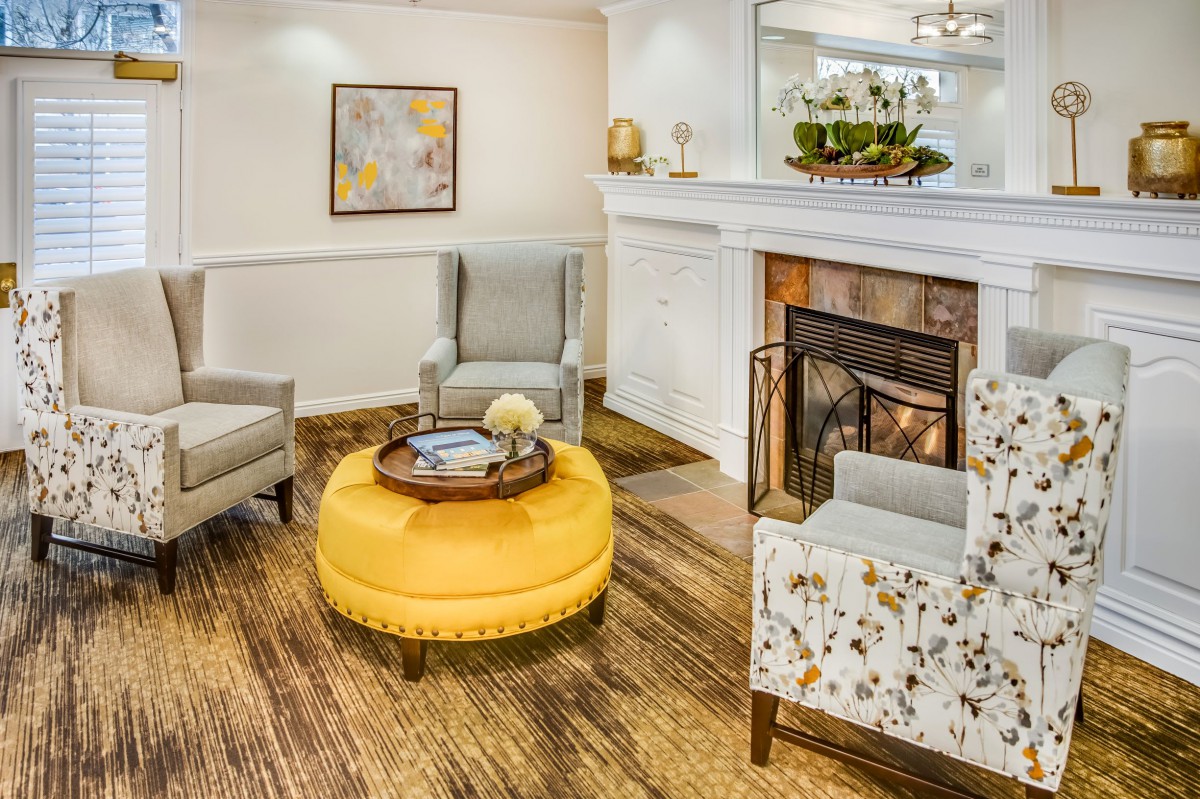 A cozy living room with a bright yellow ottoman and elegant fireplace.