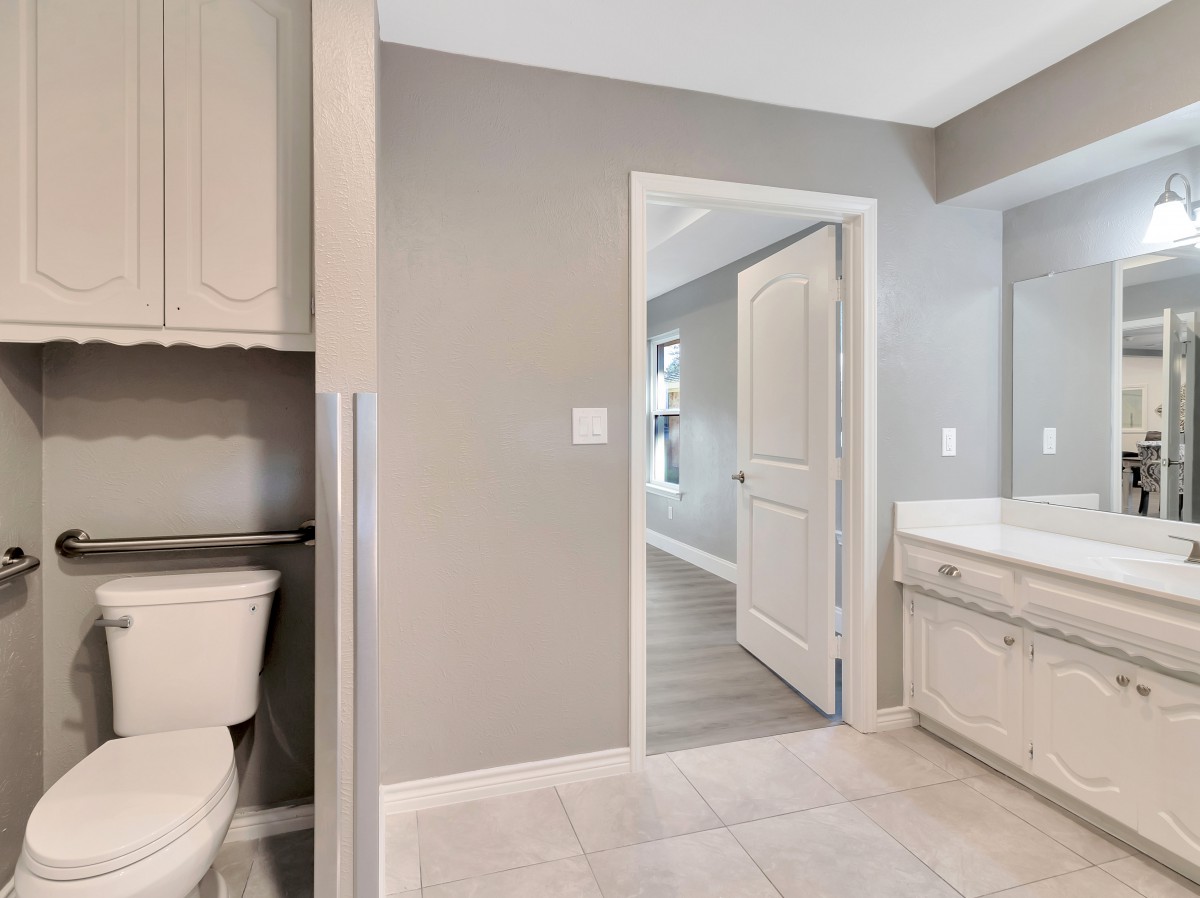 A modern bathroom featuring a toilet, sink with cabinetry, and a large mirror in neutral tones.