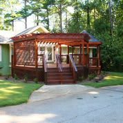 A quaint house with a wooden porch surrounded by trees and a driveway.