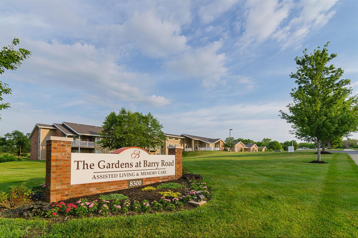 A view of an apartment complex with a sign reading 'The Gardens at Easton Road' surrounded by a well-maintained grassy landscape and a partly cloudy sky.