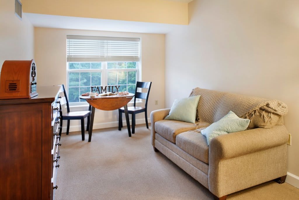 A cozy living room with a sofa, a small dining table, and a window letting in natural light.