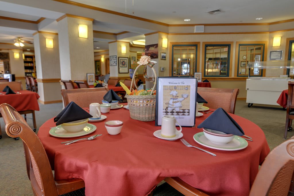 A restaurant dining setup with a red tablecloth, neatly arranged plates and cups, and a decorative basket centerpiece.