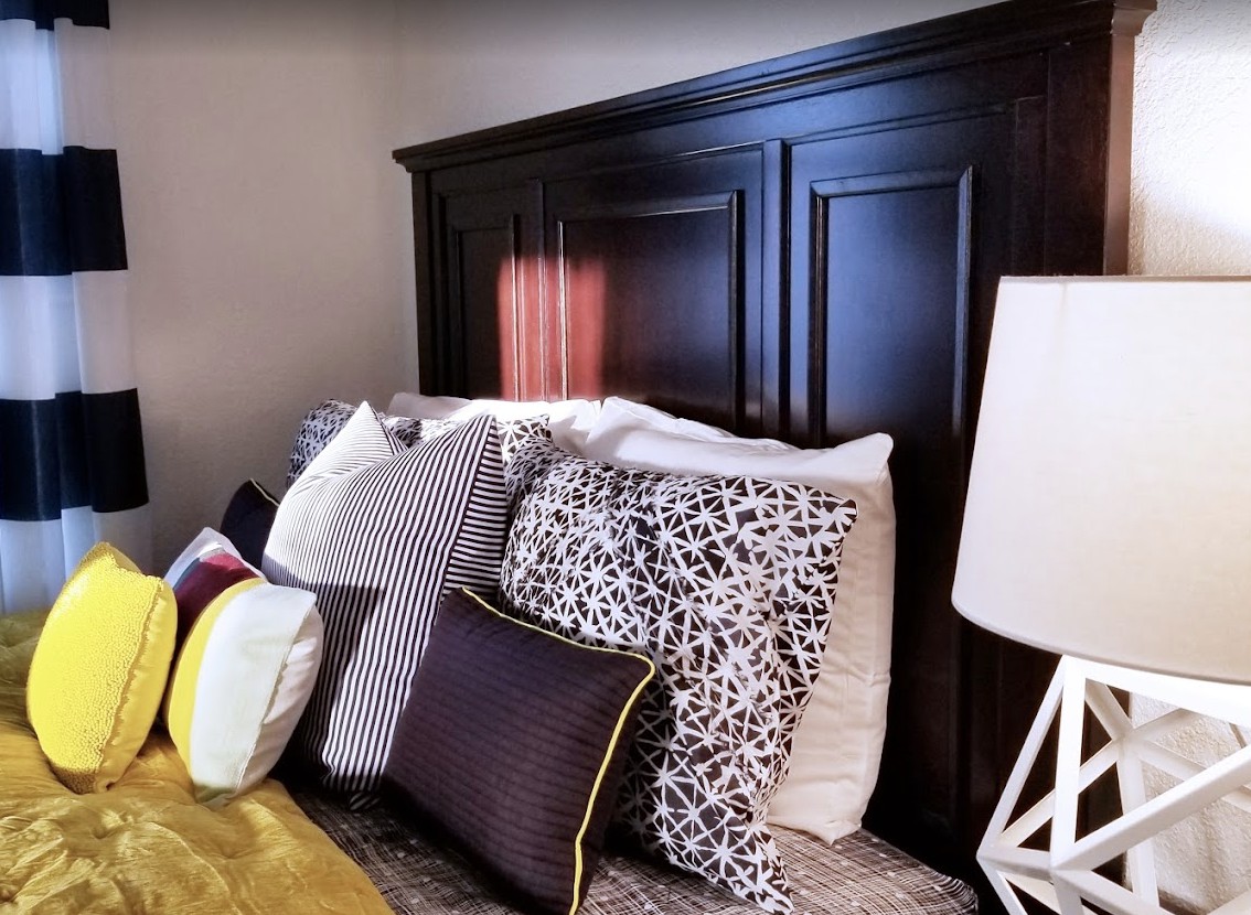 A neatly arranged bed with a variety of patterned pillows and a dark wooden headboard, complemented by a modern white lamp.