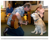 A man playing guitar for a dog in front of an audience.