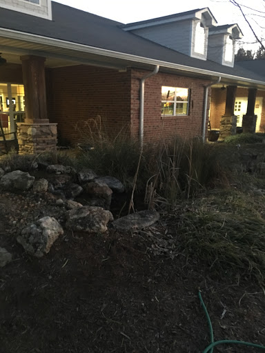 An evening view of a house with a garden featuring various plants and rock formations.