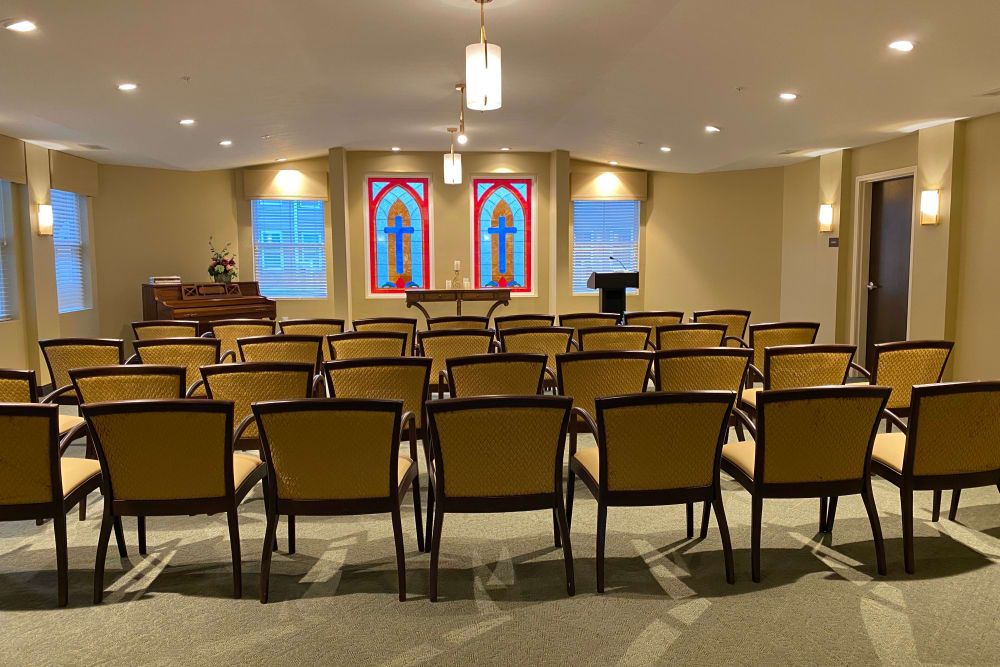 A small chapel interior with rows of chairs facing a stained glass altar.