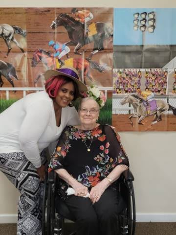 Two people smiling together in front of art, one seated in a wheelchair.
