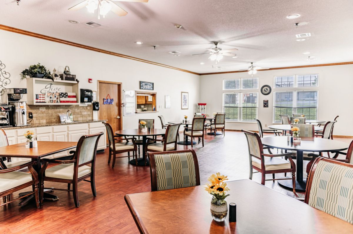 A bright and inviting dining area with multiple tables and chairs, featuring large windows and ceiling fans.