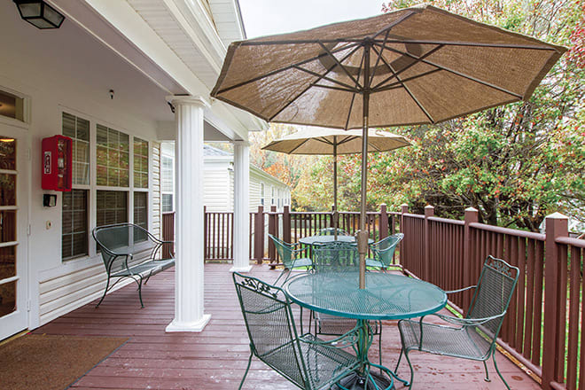 A wooden patio deck with metal furniture and large umbrellas offers a comfortable outdoor seating area amidst surrounding trees.
