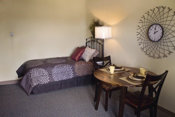 A cozy bedroom with a single bed and a small dining table, complemented by warm lighting and decorative wall art.
