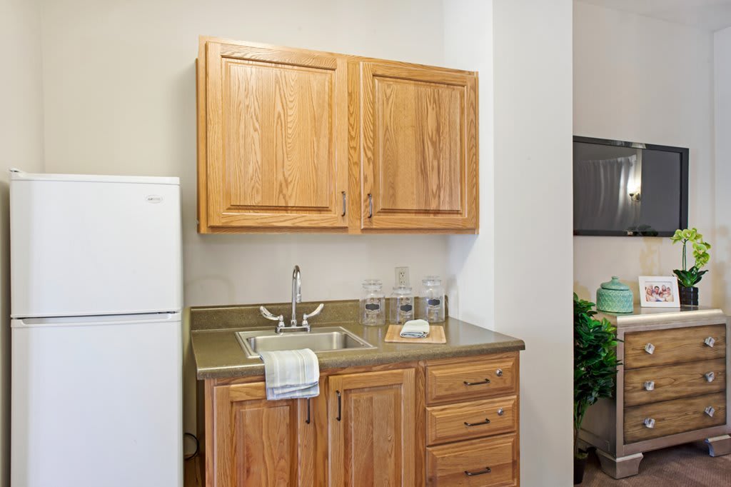 A small kitchen area featuring wooden cabinets, a sink, and a refrigerator.