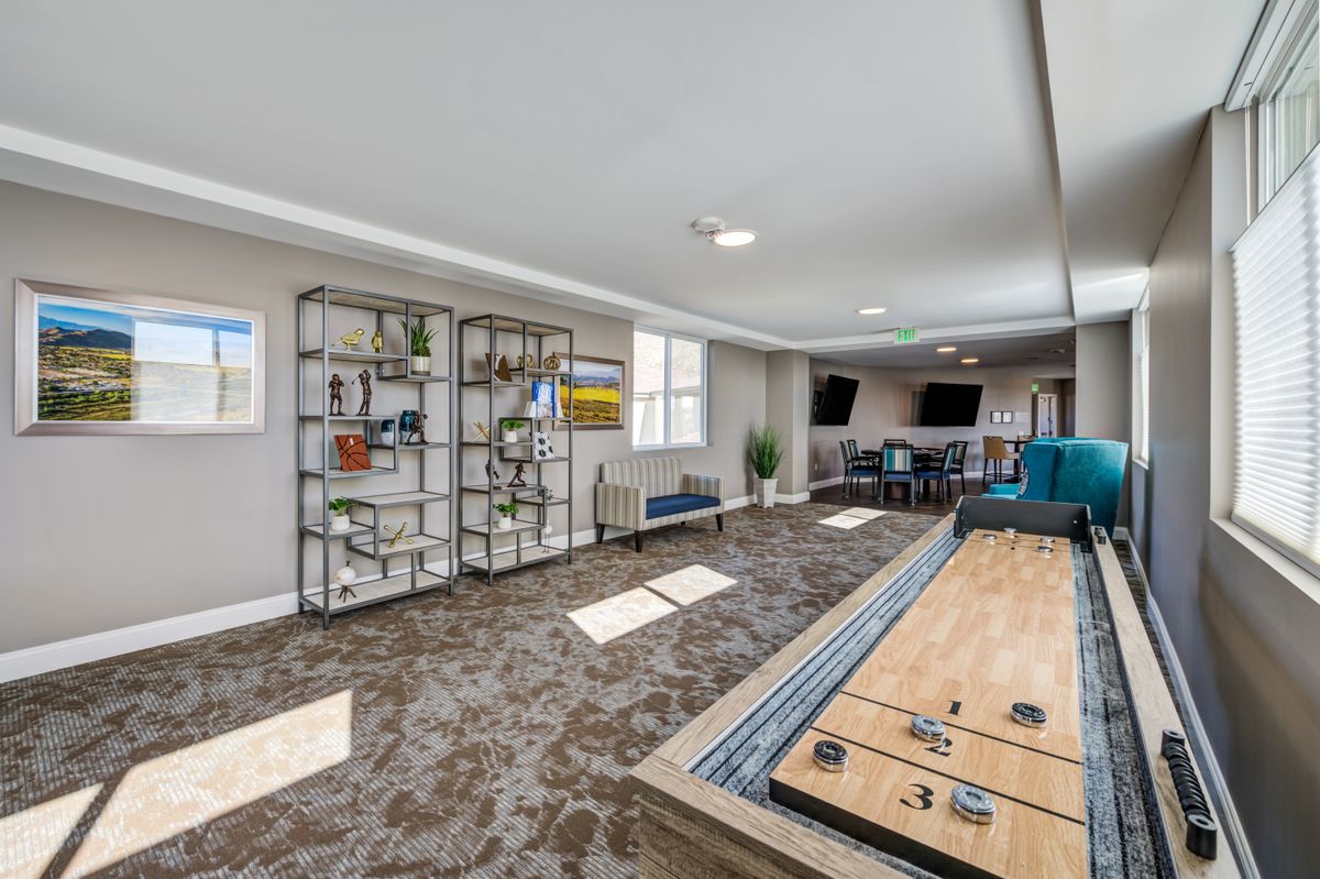 A modern game room featuring a shuffleboard table, stylish shelving, and multiple televisions.
