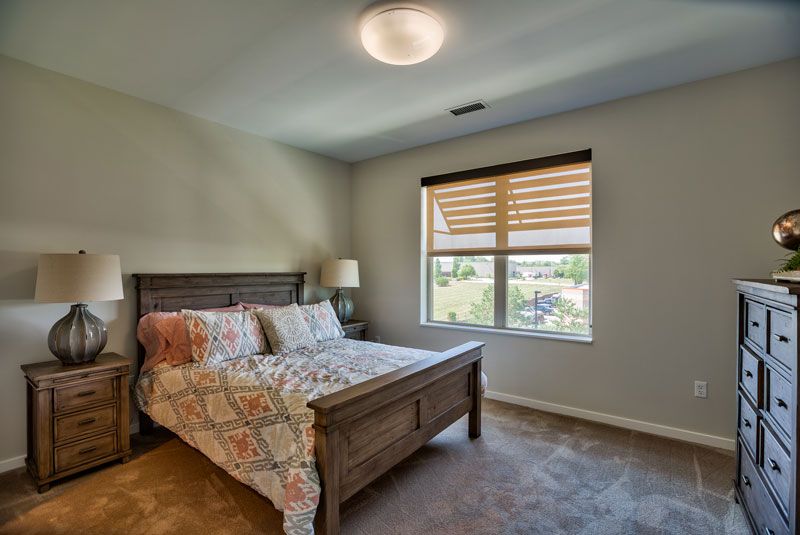A cozy bedroom featuring a bed with colorful bedding, a bedside lamp, and a window with blinds.