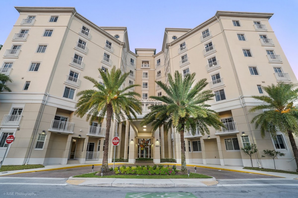 A modern apartment building with palm trees in front, showcasing urban architecture.