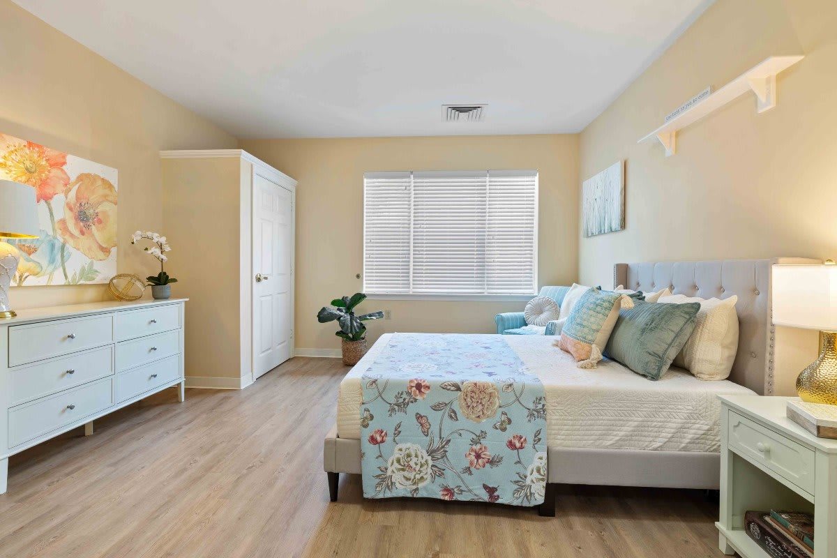 A bright and cozy bedroom with light-colored decor and wooden flooring.