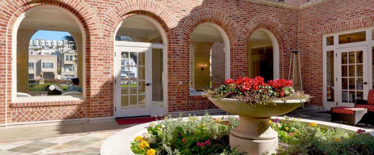 A charming brick building with arched windows and a welcoming entrance, surrounded by a colorful garden.