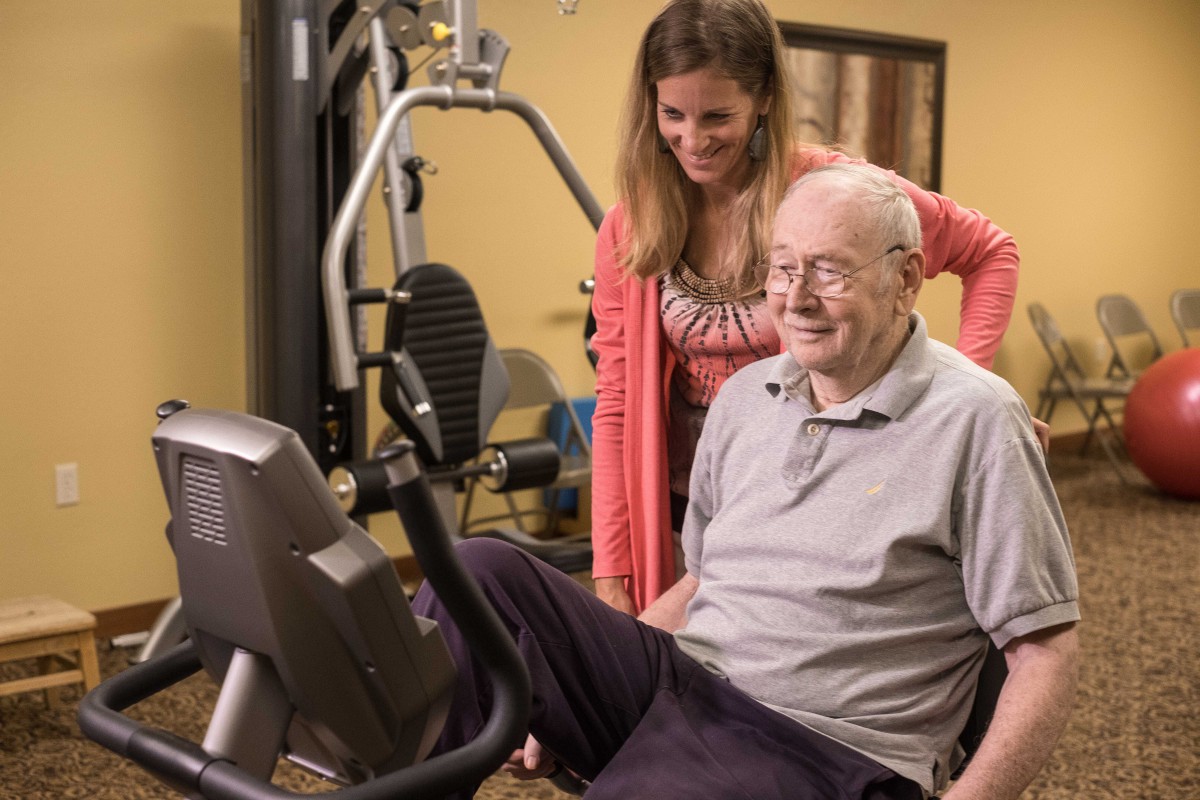 An elderly man working out with the assistance of a trainer in a gym.