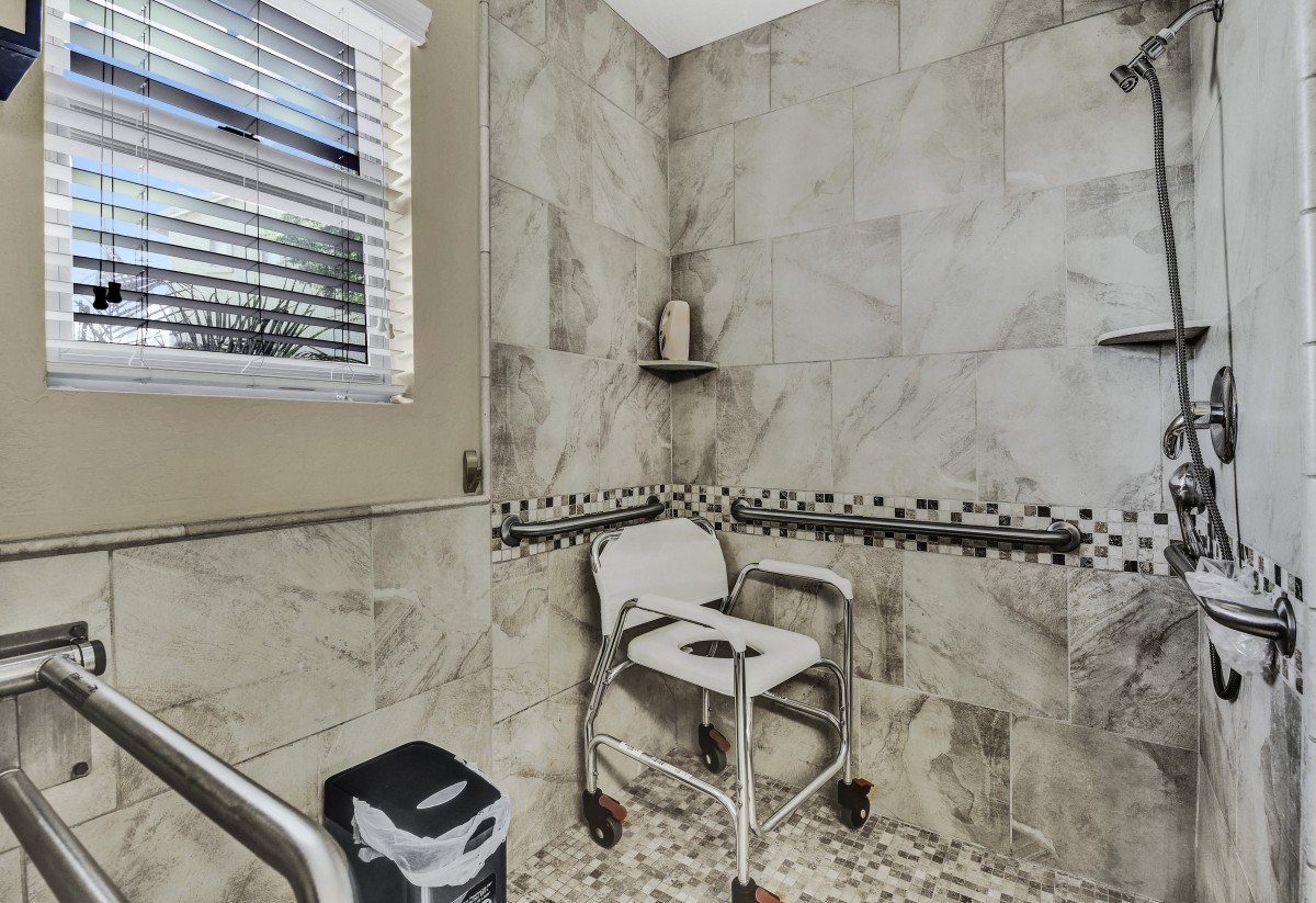 An accessible bathroom with a shower chair and tiled walls.