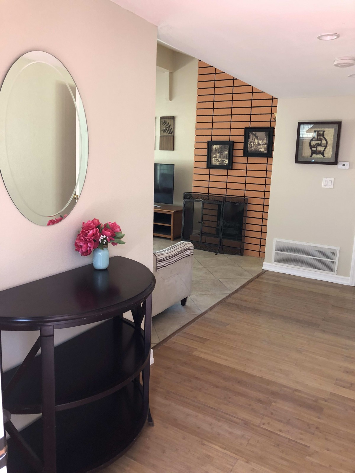 A cozy living room featuring a round mirror, vase of flowers, and artwork on a brick accent wall.