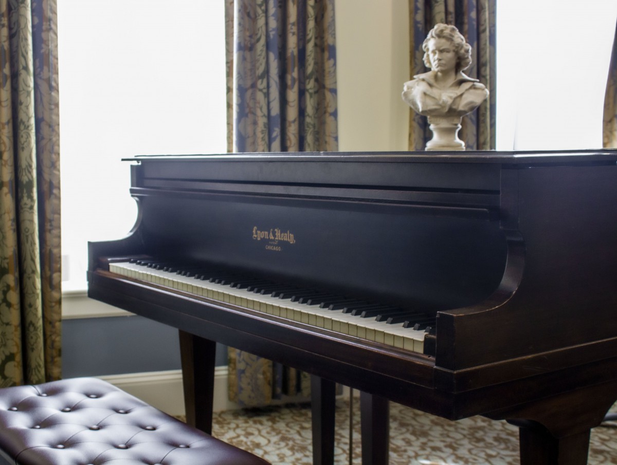A classic grand piano in a well-appointed music room, adorned with a bust on top.