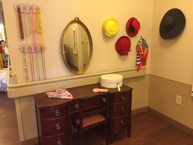 A vintage-style vanity area with hats hanging on the wall and a mirror above a wooden desk.